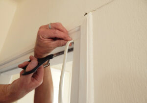 Photo of someone using draft excluder tape to seal a window frame.