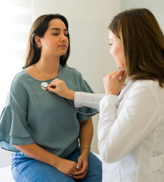 Stock photo of a woman receiving a medical check up from a doctor. The doctor is using a stethoscope.