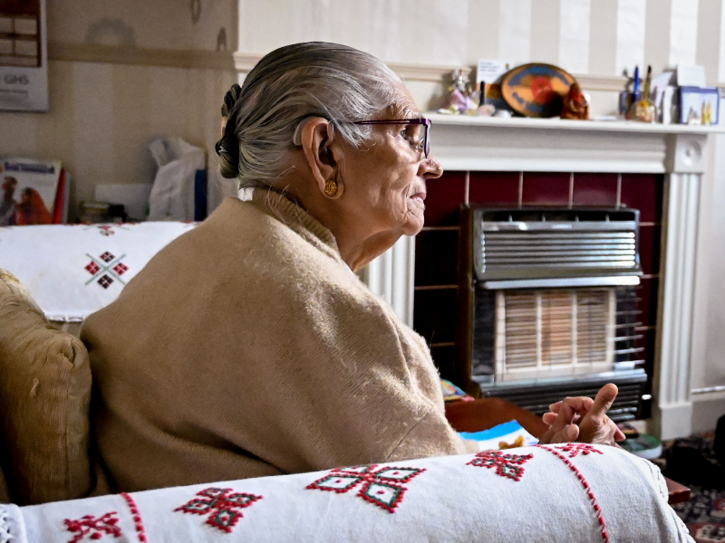 A client supported by National Energy Action. She is wearing a jumper and is sat by a heater.