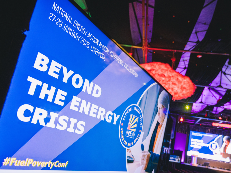 A TV screen shown at National Energy Action's Conference. The screen shows the words, 'Beyond the energy crisis' with NEA's logo and a picture of a client.