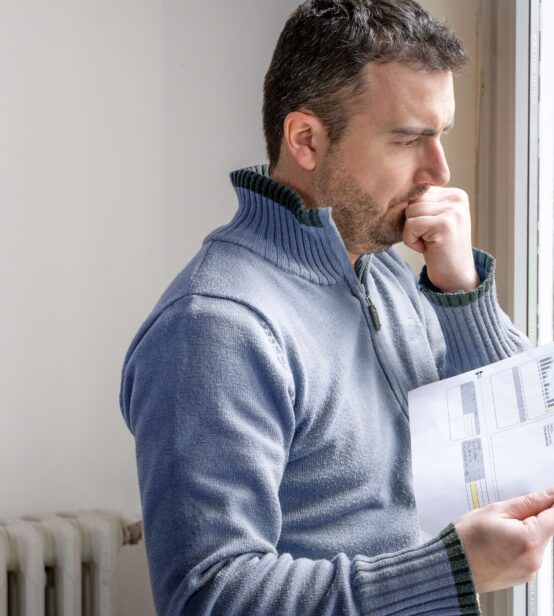 Stock photo of a man looking concerned holding an energy bill in his hand.