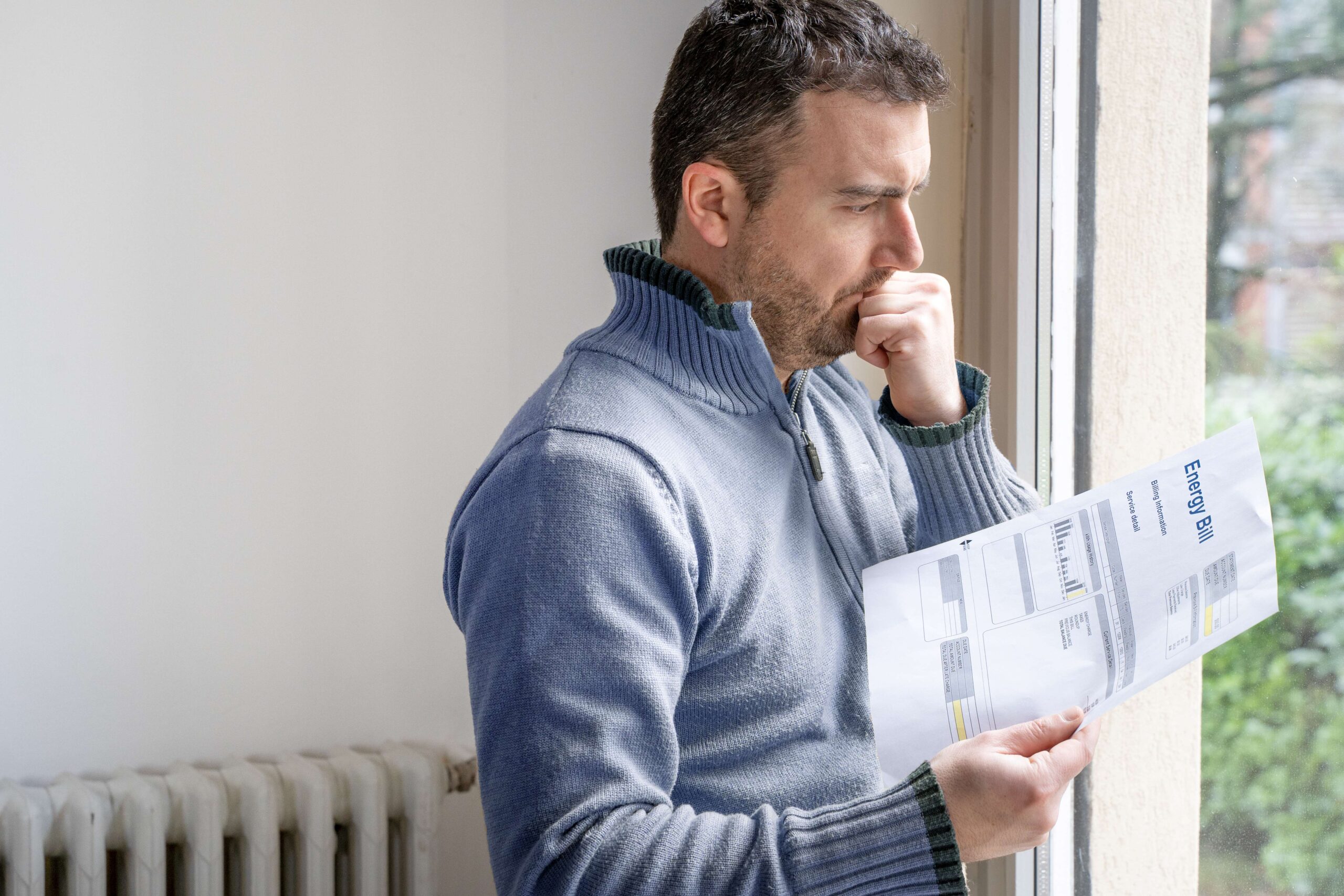 Stock photo of a man looking concerned holding an energy bill in his hand.