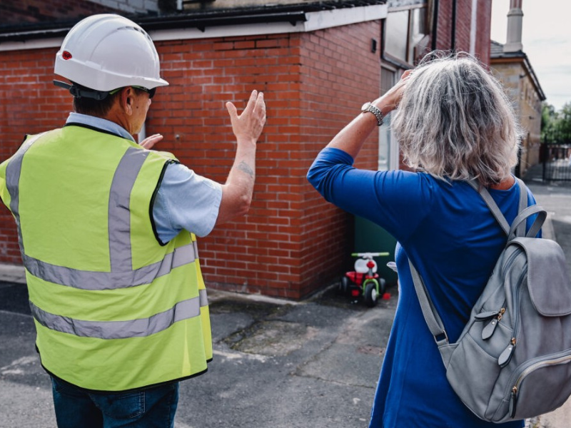 Contractor explains retrofit solutions on a terraced house. He is facing away from the camera and speaking to somebody else.