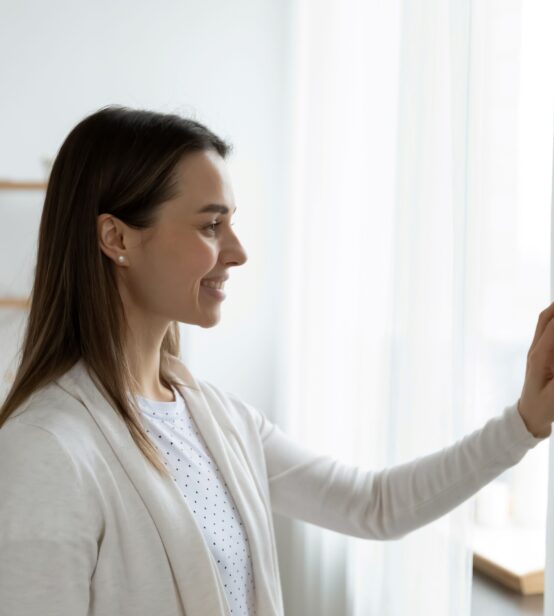 Stock photo of a smiling woman adjusting the thermostat in her bright, modern home.