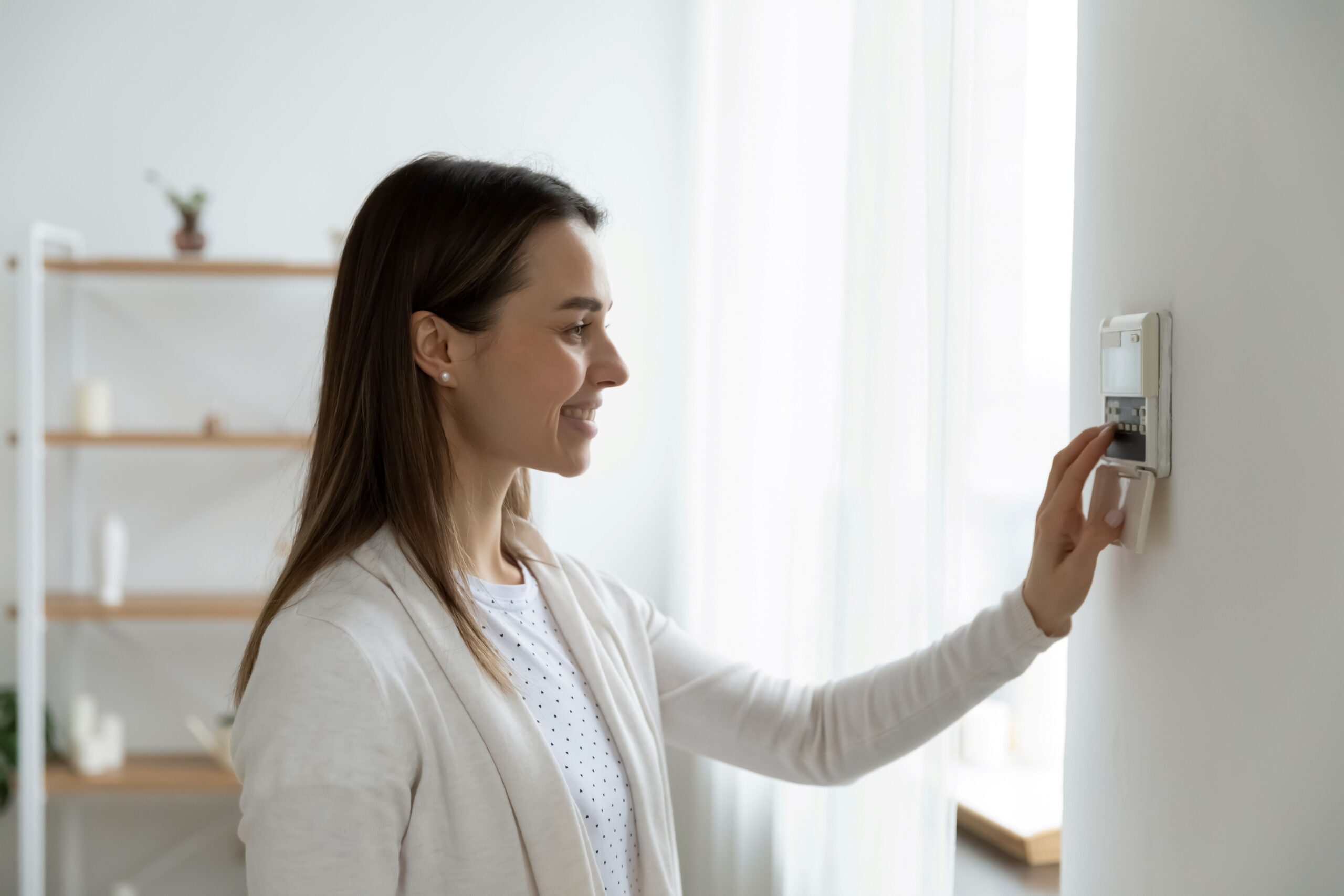 Stock photo of a smiling woman adjusting the thermostat in her bright, modern home.