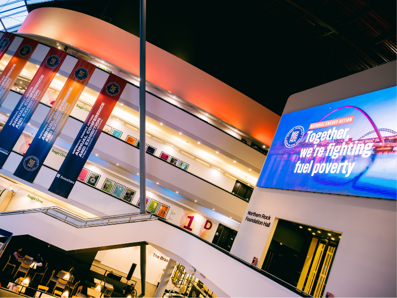 A photo of National Energy Action's fuel poverty conference. On a large screen, there's some text saying, 'Together, we're fighting fuel poverty.'