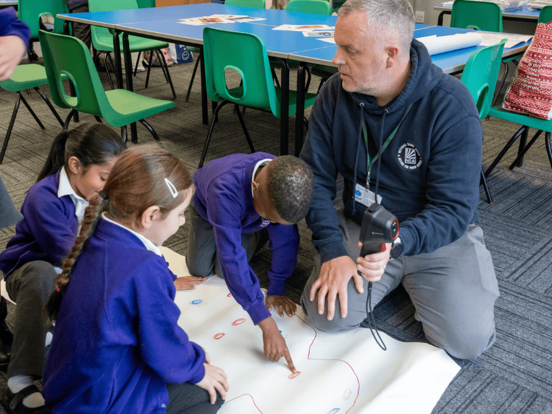 Teacher Dean helps three pupils who are wearing purple cardigans with their school work
