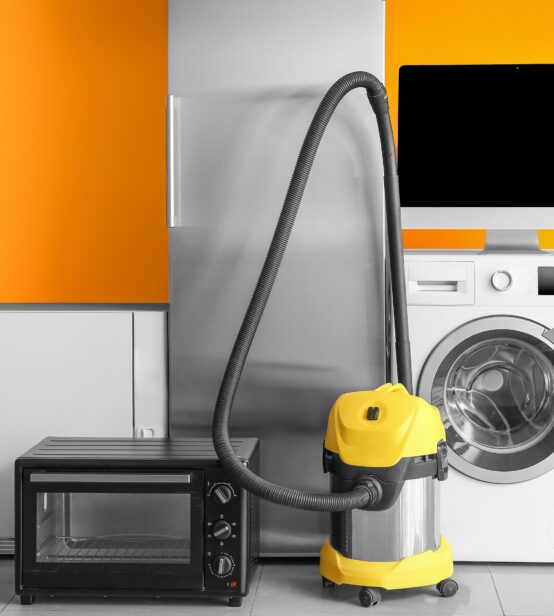 Stock photo of various electrical appliances in a home, including a microwave, washing machine, vacuum cleaner, fridge-freezer and a computer monitor.