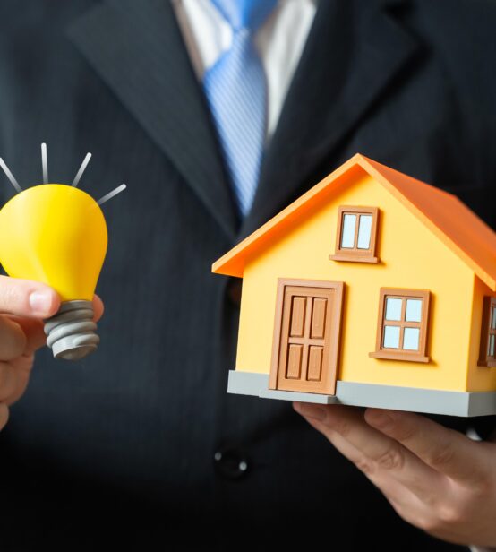 Stock image of a businessman holding a model lightbulb and a model house.