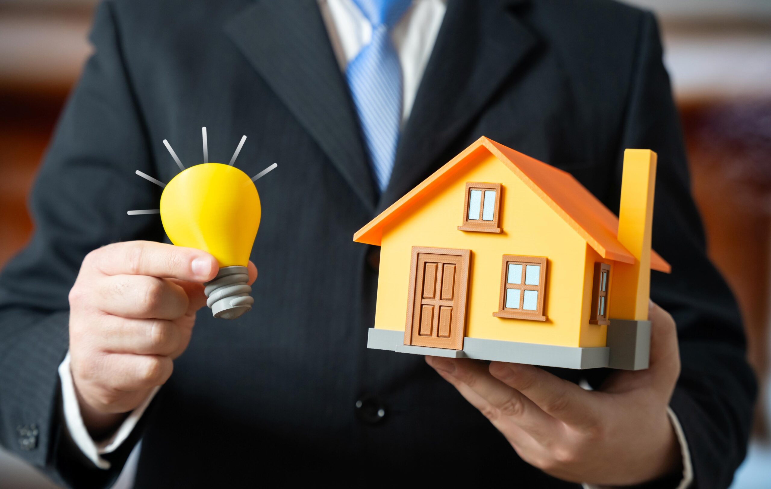 Stock image of a businessman holding a model lightbulb and a model house.