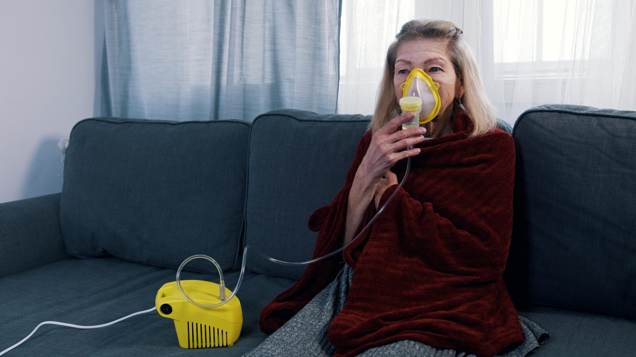 Stock photo of a woman sitting on her sofa using a breathing machine.