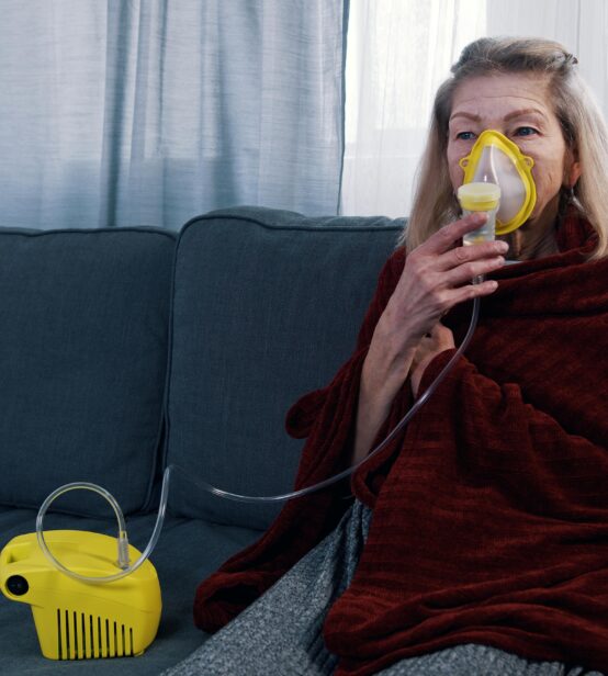 Stock photo of a woman sitting on her sofa using a breathing machine.