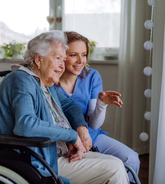Stock photo of a carer or nurse speaking to an elderly woman in a wheelchair. They are both looking out the window.