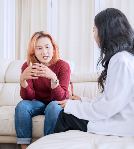 Stock photo of woman on a sofa speaking to a medical professional, who is taking notes.