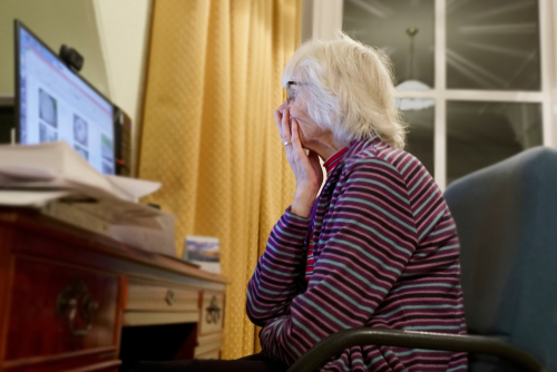 An older woman looking at a laptop looking concerned.
