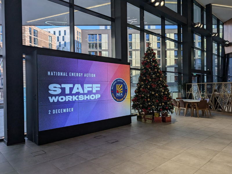 A large electronic screen that says 'National Energy Action Staff Workshop.' There is a Christmas tree next to it.