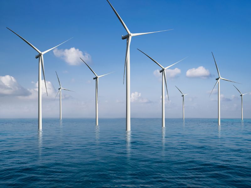Offshore wind turbines in a calm blue ocean under a partly cloudy sky