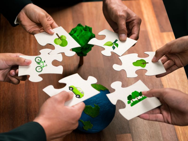 Hands holding puzzle pieces representing environmental themes over a small globe on a table