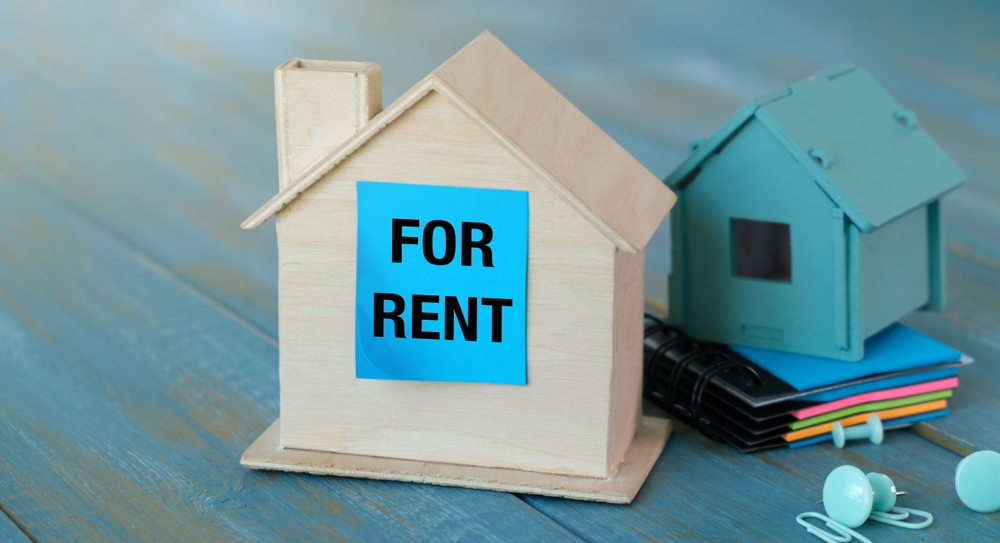 Stock photo of miniature home with a 'FOR RENT' sign on it.