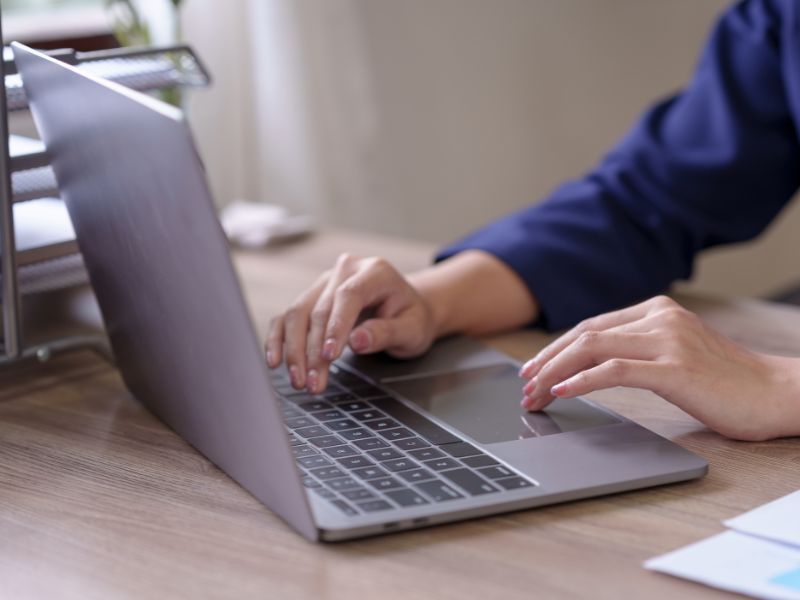 Hands typing on a silver laptop on a wooden desk