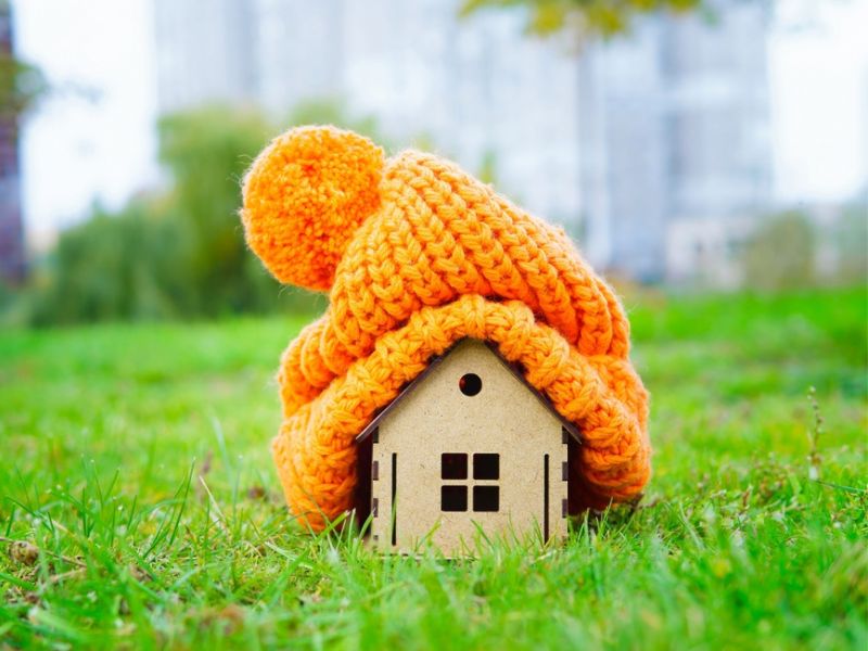 A small house sits on green grass, adorned with a colorful knitted hat resting on top of it